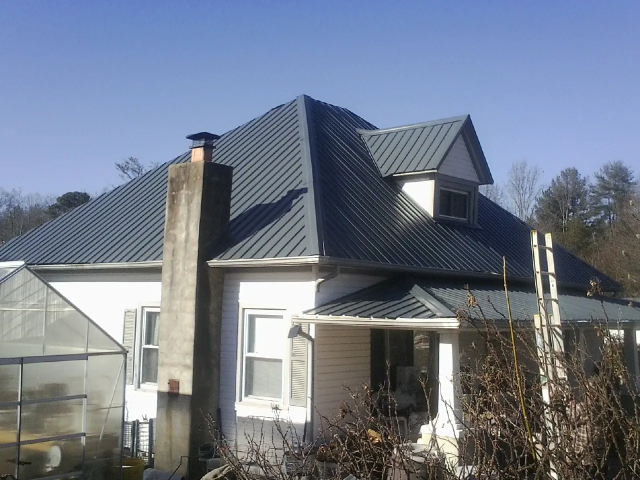 Dark blue standing seam metal roof on a white farmhouse with dormer — Slate & Tile Roof Repair by Roofing Brothers in Hospers