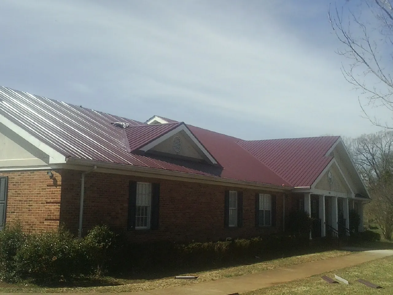 Red metal roof with gabled entries on a long brick building, from a Hail Damage Roof Repair job in Hospers
