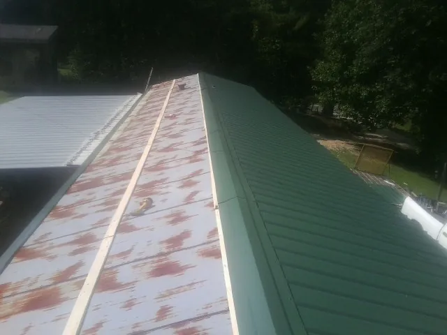 Old rusted panels beside newly installed green metal roofing — Wind Damage Roof Repair by Roofing Brothers in Hospers
