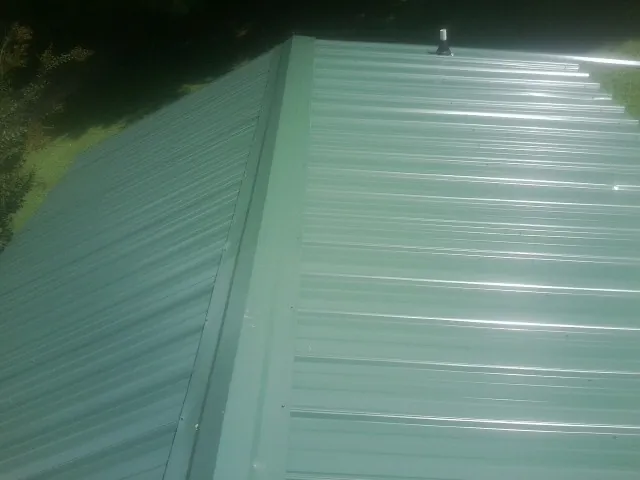 New green metal panels meeting at the ridge of a roof — Flat Roof Repair work by our crew in Hospers