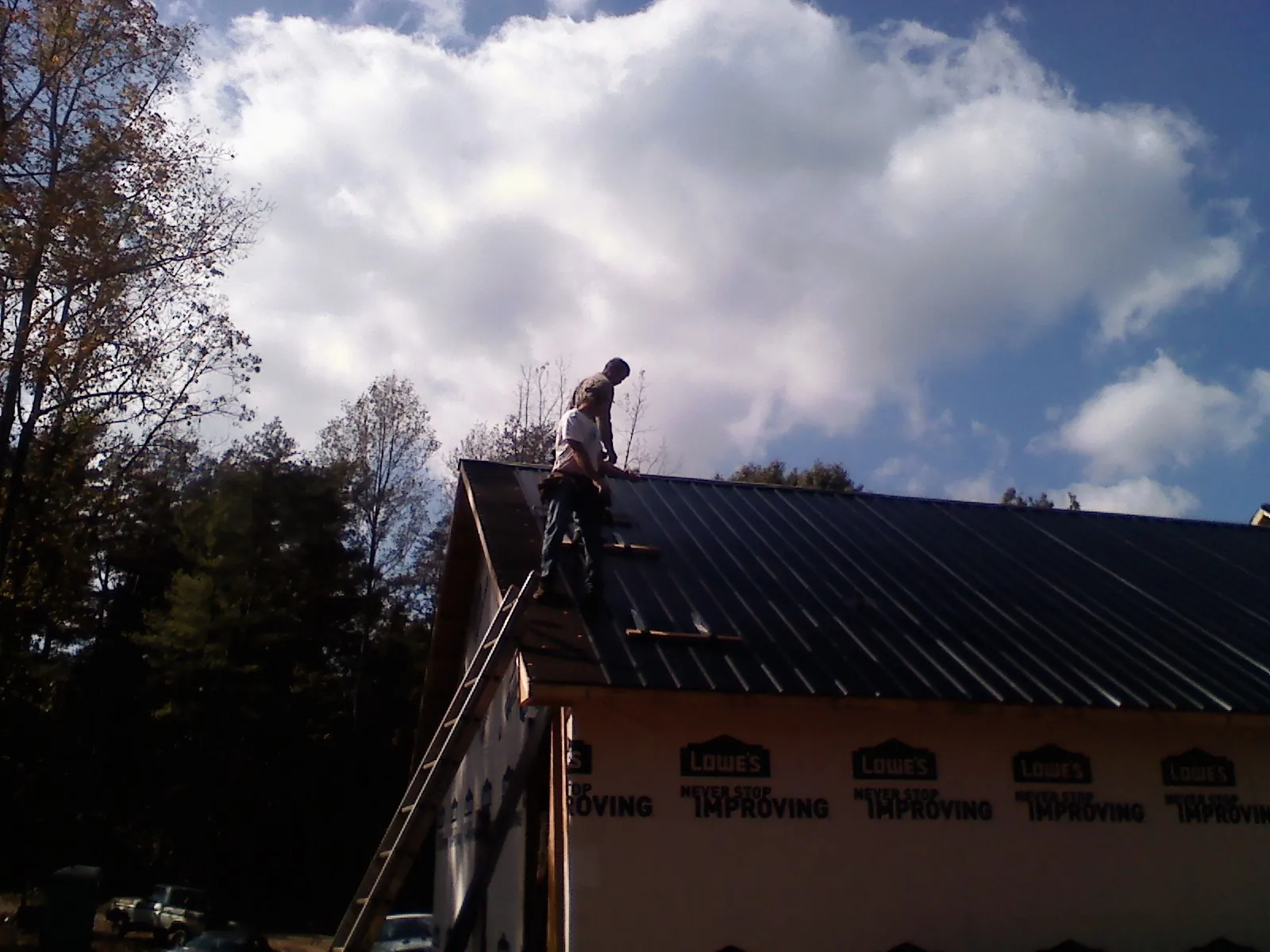Roofer fastening dark metal panels high against a cloudy sky, from a Roof Inspection job in Hospers