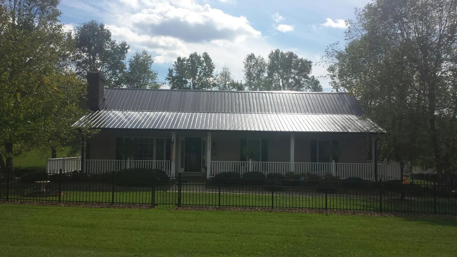 Gray metal roof on a brick ranch with a full width front porch — Gutter Guard Installation work by our crew in Hospers