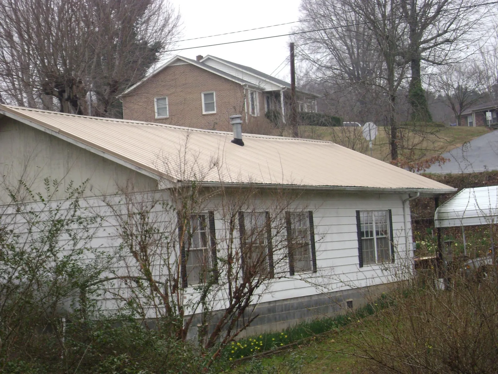 Tan metal roof on a white sided house set into a hillside — Commercial Roofing by Roofing Brothers in Hospers