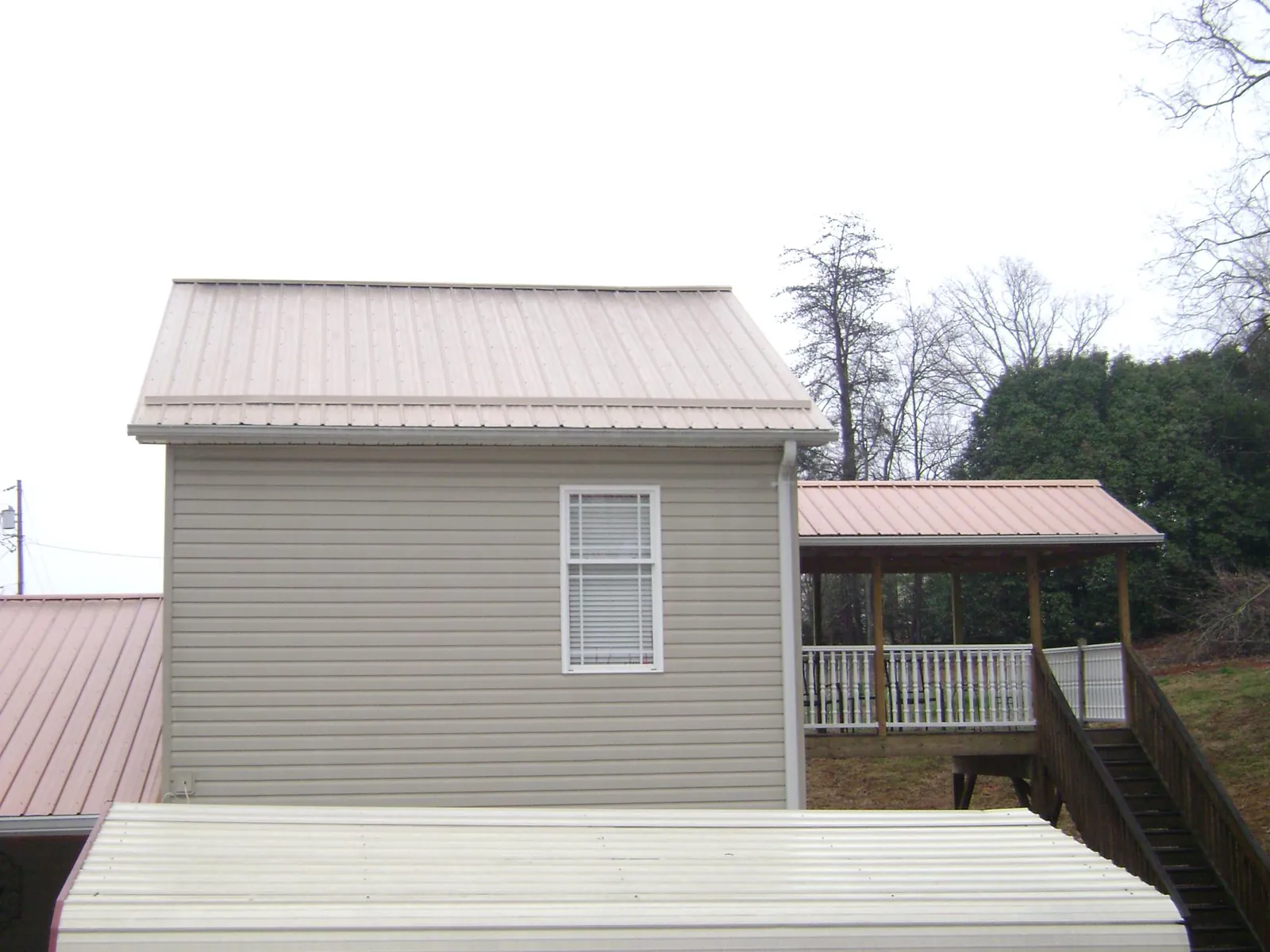 Tan metal roofs on a two story addition and attached porch, from a Roof Replacement job in Hospers